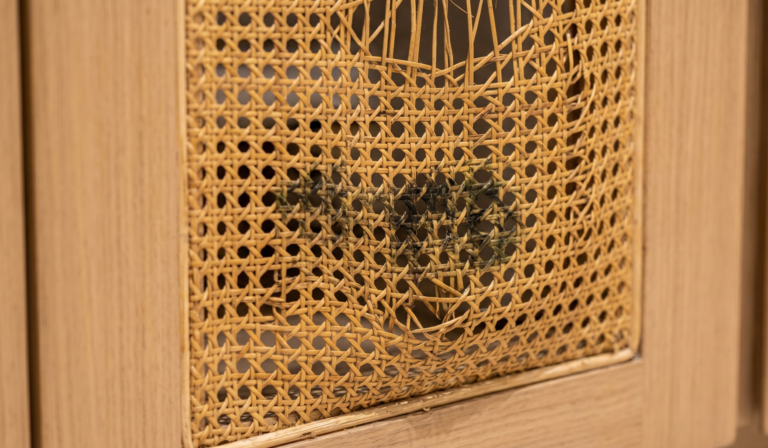 Sagging rattan webbing with dark fungus spots inside a light oak cabinet frame.