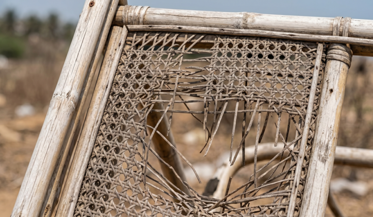 Weather-damaged and broken rattan webbing on an outdoor frame exposed to harsh sunlight and rain.