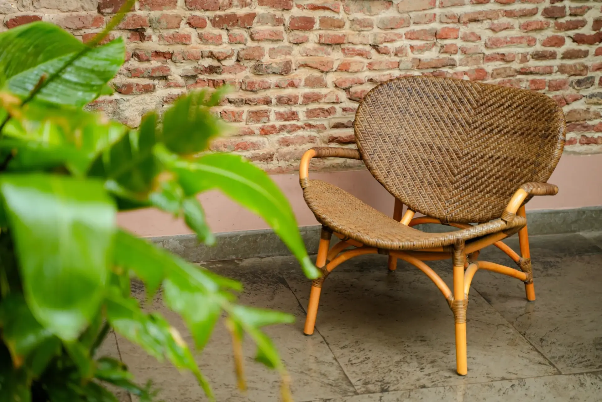 Handcrafted rattan chair featuring a detailed woven herringbone pattern against a raw brick wall.
