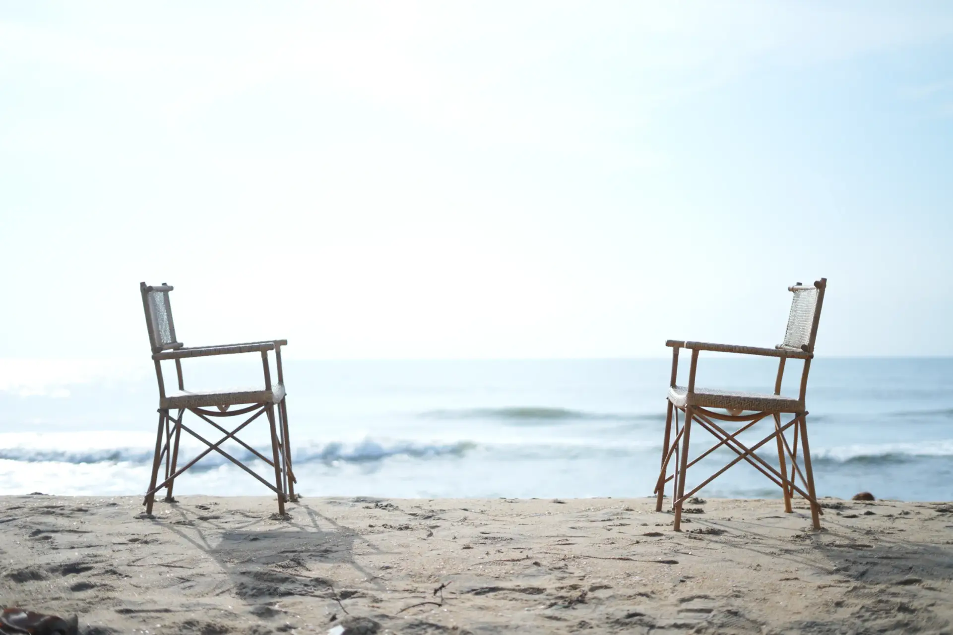 Two handcrafted rattan armchairs facing each other on a bright sandy beach.